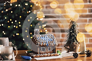 Gingerbread house on Christmas table with decorations, candles in living room