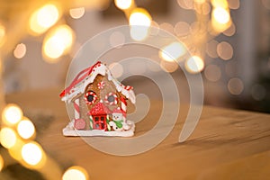 Gingerbread house. Nice souvenir. Gift. On a wooden surface against the background of blurred Christmas lights