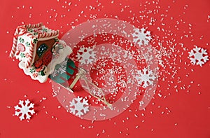 Gingerbread house on a sled on a red background with snow and snowflakes. Christmas background. Christmas and New Year concept.