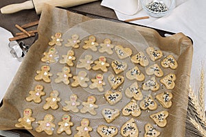 Gingerbread man and cookie hearts on baking paper on a baking sheet on a wooden table. The scene of making homemade pastries