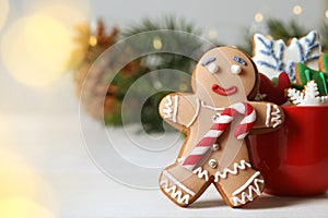 Gingerbread man and delicious homemade Christmas cookies on white wooden table against blurred festive lights. Space for text
