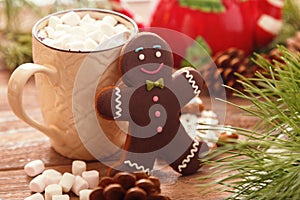 Gingerbread man and hot chocolate with marshmallows, on the background of Christmas tree branches on a wooden table
