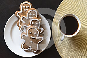 Gingerbread men on a white plate on black background with a cup coffee