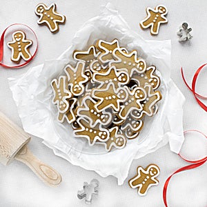 Gingerbread men on a white tablecloth next to a red ribbon and cookie cutters.