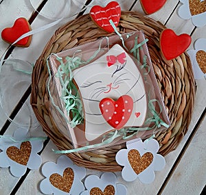 Gingerbread with a mural. Valentine`s Day. Cat with a heart and a bow on a white wooden background.