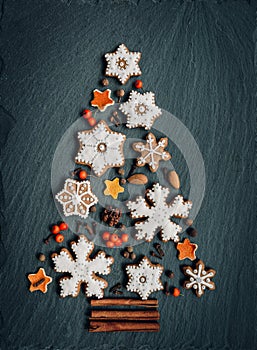 Gingerbread, nuts, spices, dried orange peel create a Christmas tree on a dark stone background