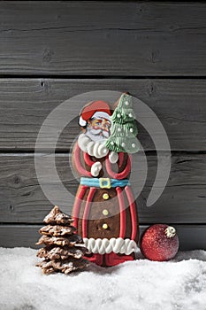 Gingerbread santa claus christmas bulb chocolate christmas tree on heap of snow against wooden background