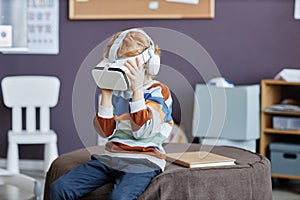 Gingerhaired little boy in striped pullover and vr headset playing virtual game