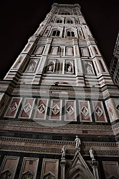 Giotto`s bell tower illuminated, which stretches towards the black background of the evening sky, in Florence.