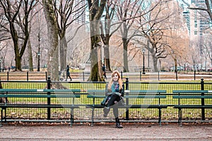Gir sitting on a bench l in front of trees at the Central Park i