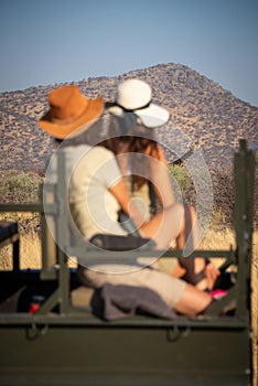 Giraffe watches two women sitting in jeep