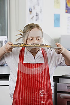 Girl (10-12) with Down syndrome carrying cookies on baking sheet in kitchen