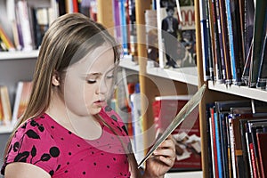 Girl (10-12) with Down syndrome holding book at bookshelves