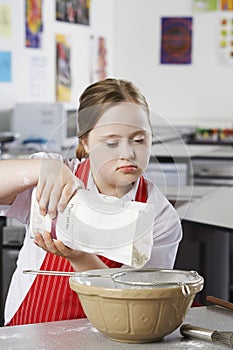 Girl (10-12) with Down syndrome pouring flour into bowl