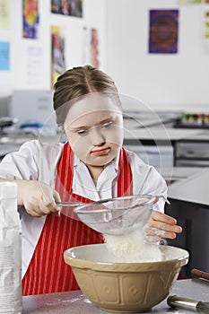 Girl (10-12) with Down syndrome sieving flour into bowl