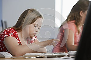 Girl (10-12) with Down syndrome using computer in computer lab children in background