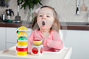 Girl 2 years old with long hair playing with designer construction at home, yawns.