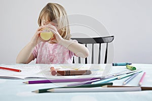 Girl (3 4) drinking orange juice crayons in foreground