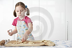 Girl (5-6) cutting dough on board in kitchen