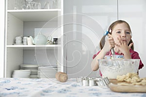 Girl (5-6) preparing food in bowl using wire whisk and licking finger