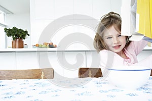 Girl (5-6) sitting at table with bowl and box of cereal