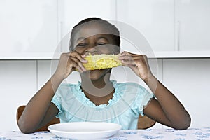 Girl (5-6) sitting at table eating corn cobb