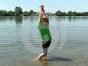 Girl 6 - 7 years old plays with water in the river. The child is wearing a green T-shirt and black shorts. Summer on the pond.