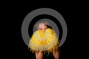 A girl of 6 years, on a black background. A cheerleader with yellow pumpons.Sport and energy.