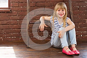 Girl 6 years old sits on the floor next to a brick wall and filled with laughter