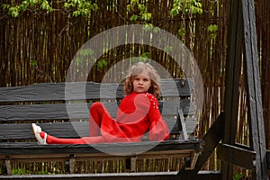 Girl 7 years old in red clothes on the street on a swing. Spring, nature, childhood