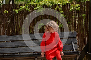 Girl 7 years old in red clothes on the street on a swing. Spring, nature, childhood