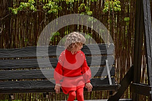 Girl 7 years old in red clothes on the street on a swing. Spring, nature, childhood