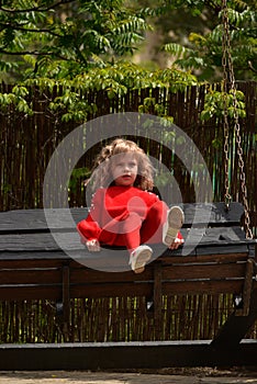 Girl 7 years old in red clothes on the street on a swing. Spring, nature, childhood