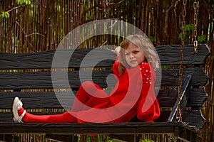 Girl 7 years old in red clothes on the street on a swing. Spring, nature, childhood