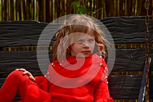 Girl 7 years old in red clothes on the street on a swing. Spring, nature, childhood