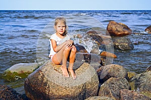 Girl 7 years old on the rocks on the beach posing .