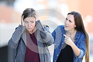 Girl accusing her sad friend in the street