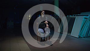 Girl addict sitting on a chair in a dark room doing an injection with drugs