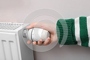 Girl adjusting heating radiator thermostat near white wall indoors, closeup