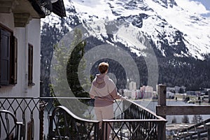 The girl admires the beautiful view of the Alpine mountains and cottages of the resort town. St Moritz, Switzerland May 2023