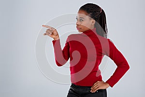 A girl, Afro-American, with a pensive look looks to the side showing the index finger in front of her.