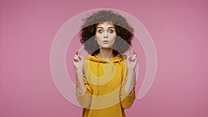 Girl afro hairstyle in hoodie standing with her eyes closed, holding good luck gesture and mentally craving