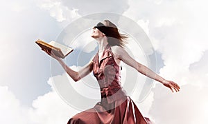 Girl against cloudy sky with opened book in palm as idea for kno