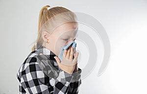 A girl aged seven years old in a checkered shirt blows her nose into a handkerchief on a white background. The concept