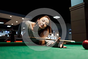 Girl aims to hit the ball while playing billiards