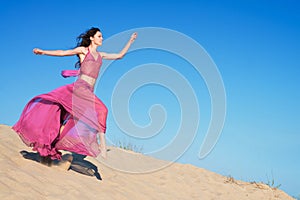 Girl in airy crimson dress running on sand dunes