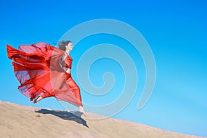 Girl in airy red dress running on sand dunes photo