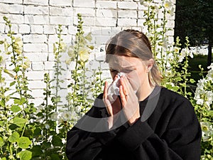 A girl with allergies sneezes into a handkerchief on the street among flowers, the concept of allergic reactions photo