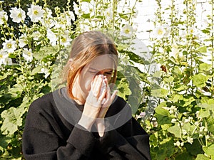 A girl with allergies sneezes into a handkerchief on the street among flowers, the concept of allergic reactions