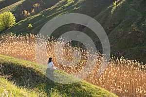 A girl alone enjoys the silence and beauty of nature, sitting on a hill in a picturesque place